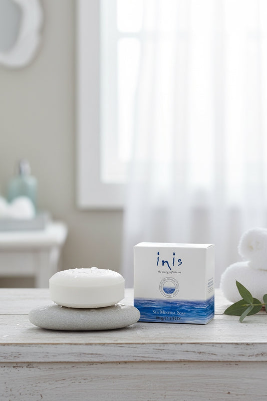Inis Sea Mineral Soap 100g bar resting on a grey pebble with box on white wooden surface alongside white towel