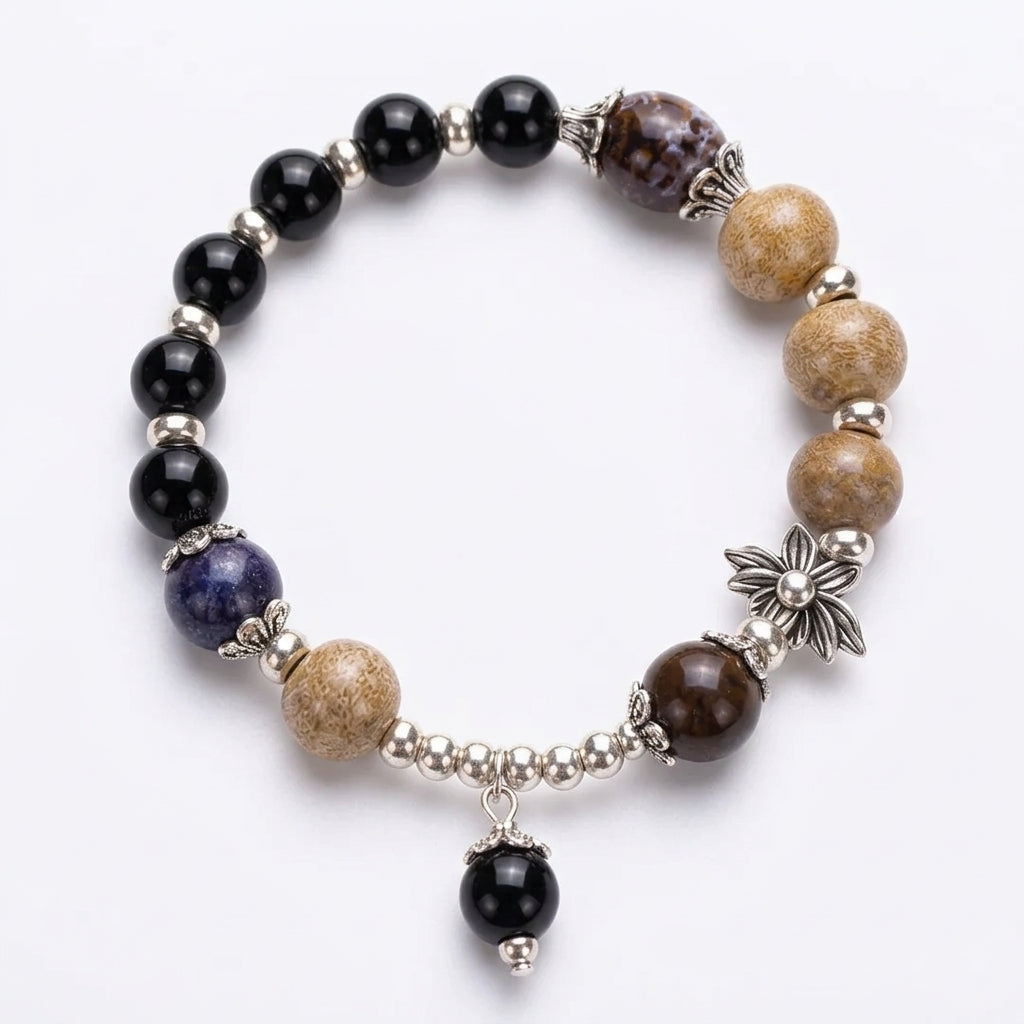 A beaded stretch bracelet featuring black onyx beads, natural brown and beige jasper stones, a blue lapis lazulii bead, and silver-toned metal spacers and charms, including a flower and a dangling black bead.