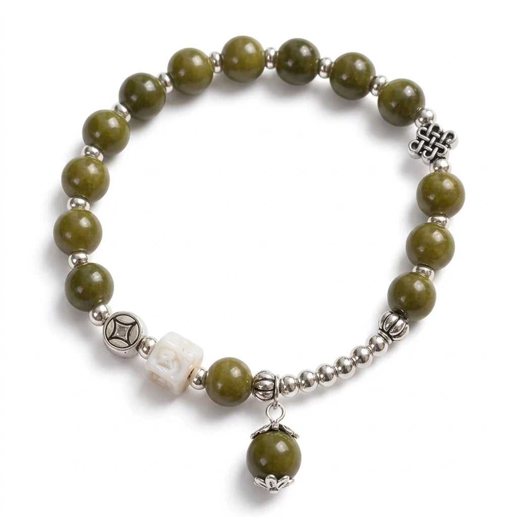 A beaded stretch bracelet featuring olive green stone beads, silver-toned spacer beads, a white carved accent bead, a dangling green bead charm, and silver decorative charms, shown on a white background.